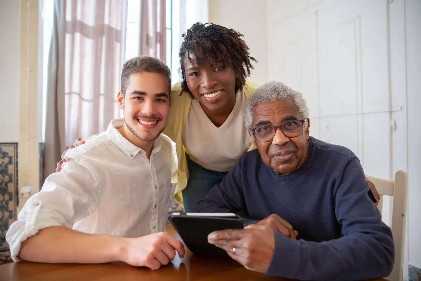 Two carers smiling with an elderly man at his dining table