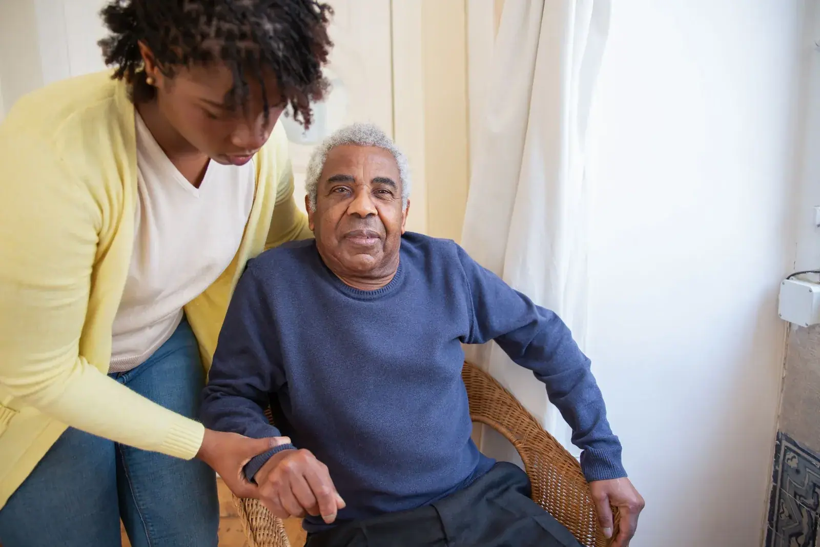 A carer helping an elderly man up from his armchair