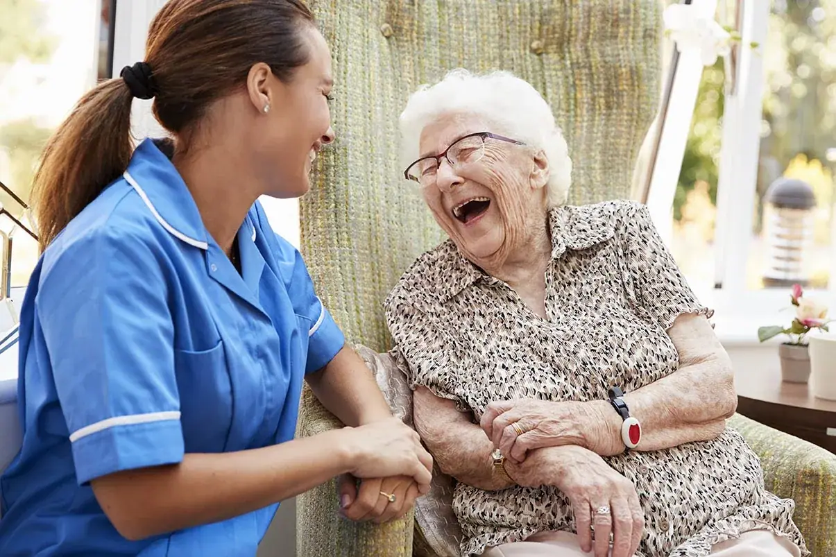 A carer laughing with an elderly woman in a care chair