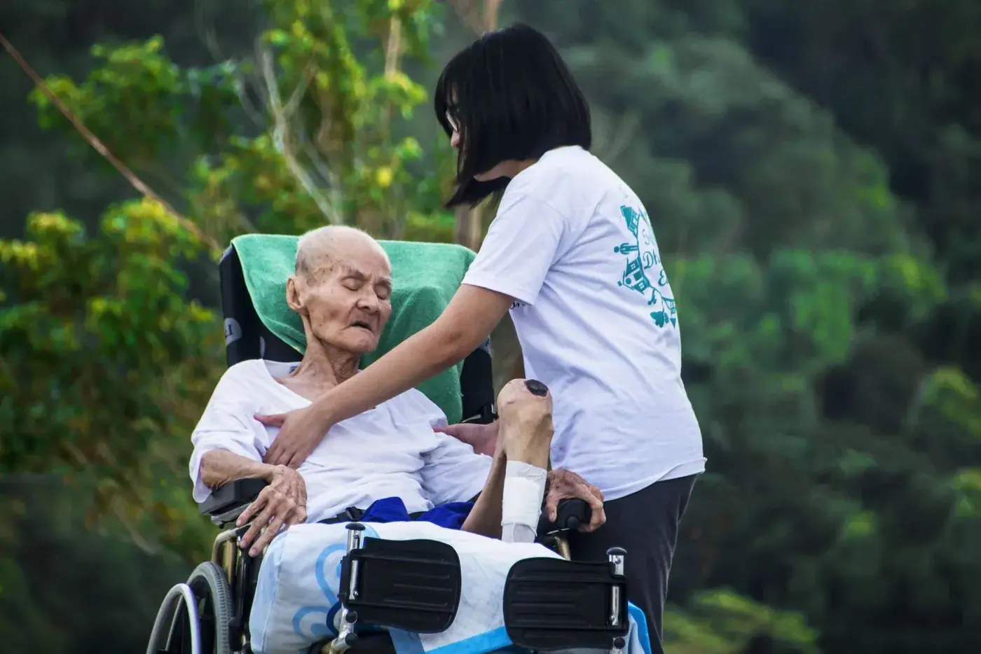 A carer helping an elderly man in a wheelchair outdoors